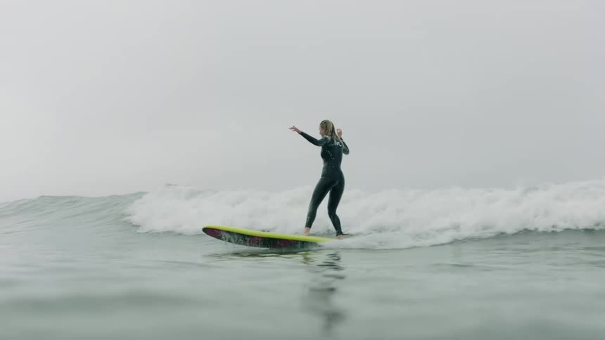 A female surfer gracefully rides a wave in slow motion on a summer day, filmed from a beautiful water-level perspective