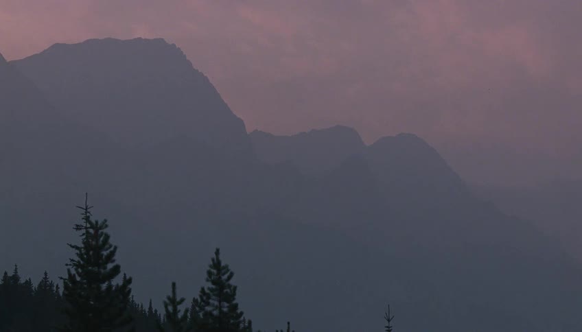 Hazy mountain peaks are silhouetted against a moody purple sky at twilight