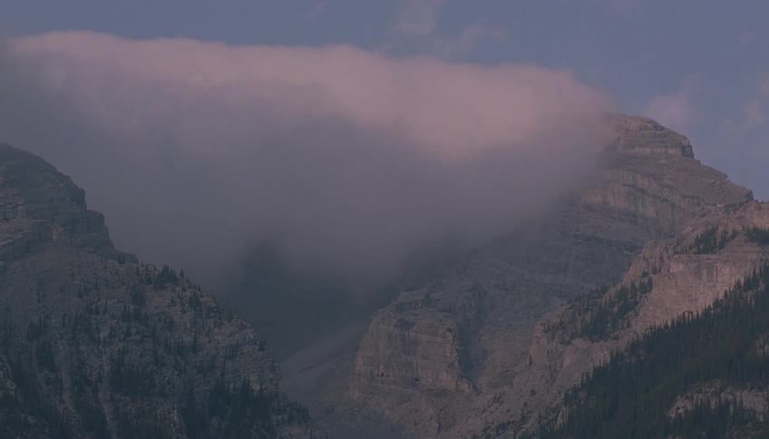 A thick, moving cloud envelopes a mountain summit