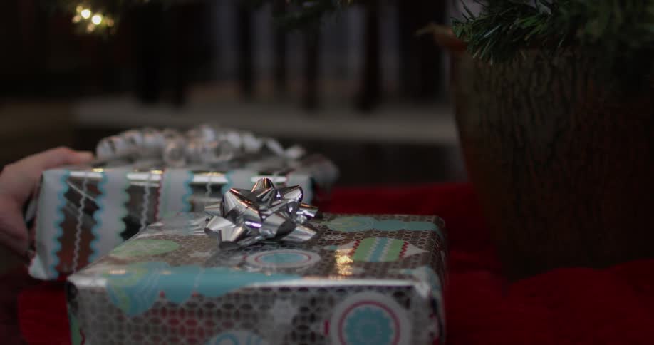 A person is placing wrapped presents under a tree at night