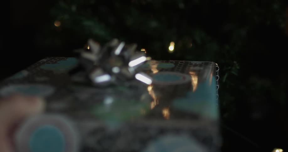 Person setting wrapped gift with bow under christmas tree