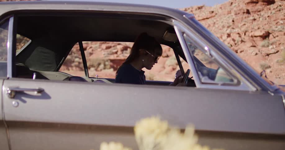 An angry woman in a vintage car repeatedly hits the steering wheel in frustration while stranded in the desert