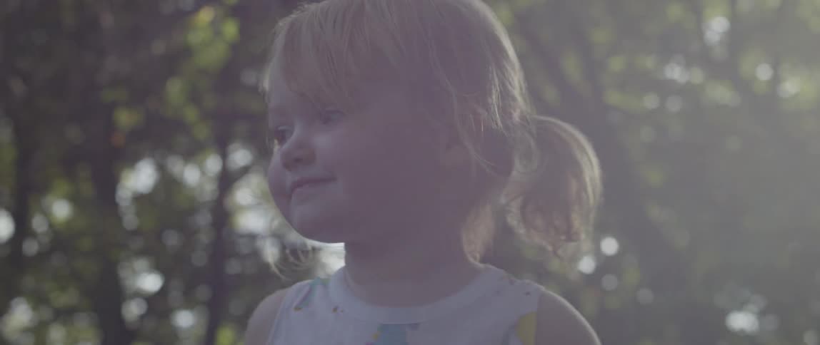 A young girl stands outside with the sun shining behind her