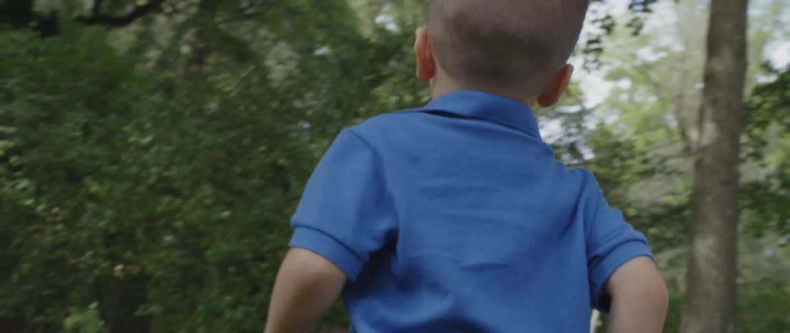 A boy races on the grass towards the trees