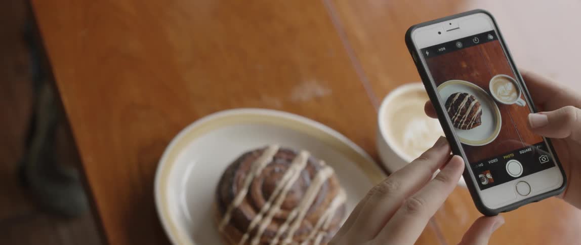 A woman photographs a cinnamon bun and coffee drink