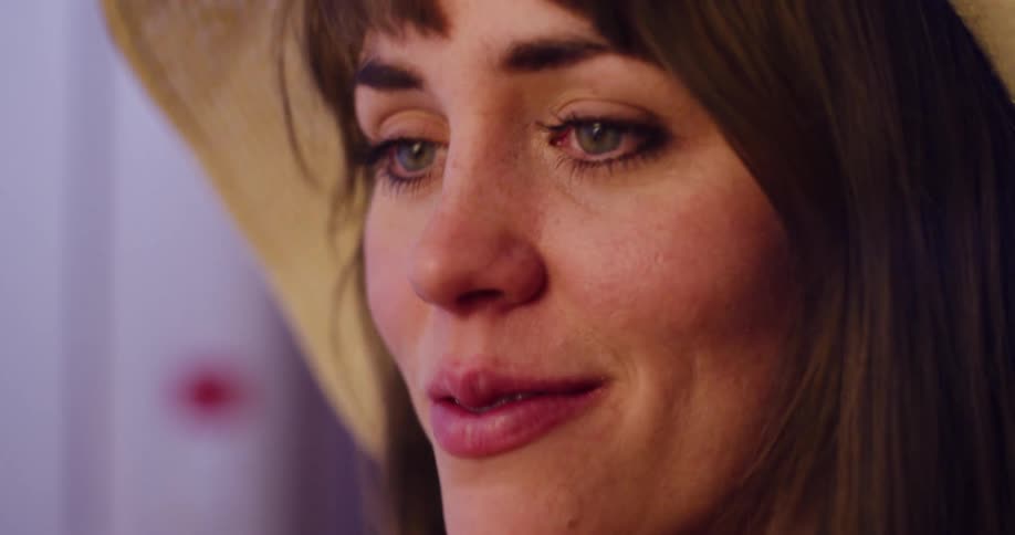 A close up of a sad woman in a straw hat with tears welling up in her green eyes as she looks off-camera
