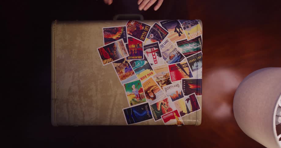 Top-down view of hands smoothing down a collage of colorful, retro travel postcards on a vintage suitcase