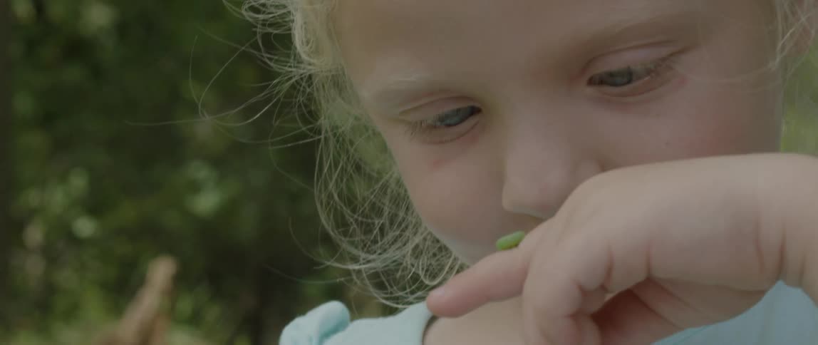 A child looks closely at a bug on her finger