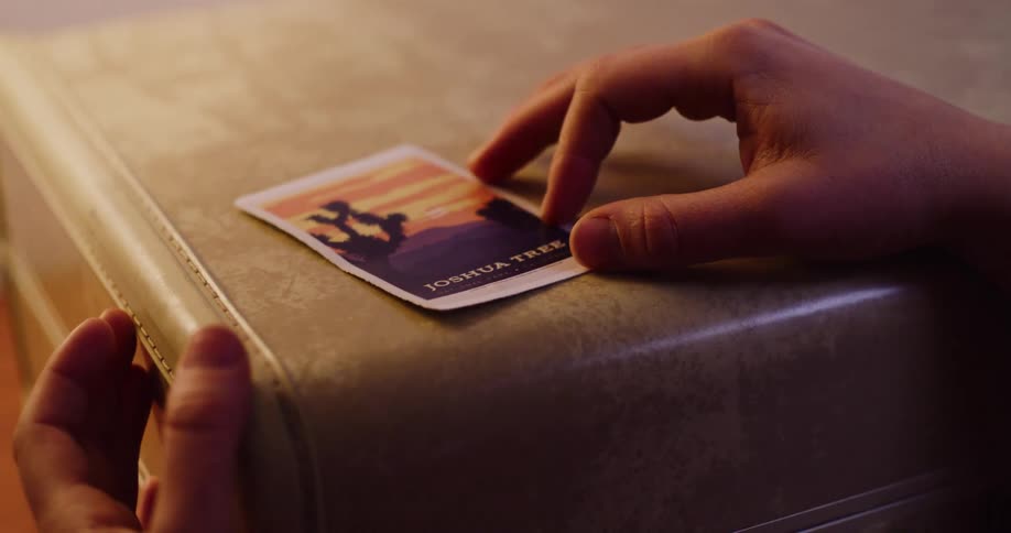 Close-up of hands applying a nostalgic Joshua Tree sticker to a vintage travel suitcase