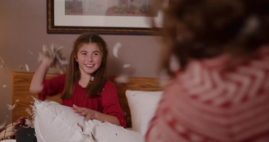 Slow motion shot of a joyful young girl having an epic pillow fight on a bed as feathers fly all around her