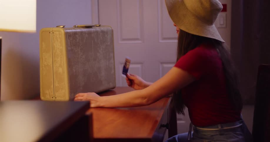 A young traveler in a sun hat adds a postcard to her collection on a vintage suitcase inside her hotel room