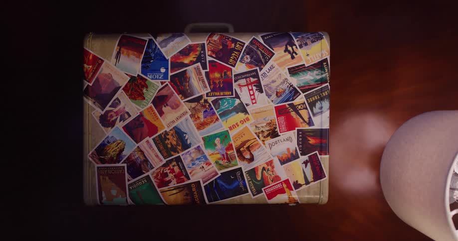 A looping cinemagraph shows a suitcase covered in travel postcards resting on a wooden floor