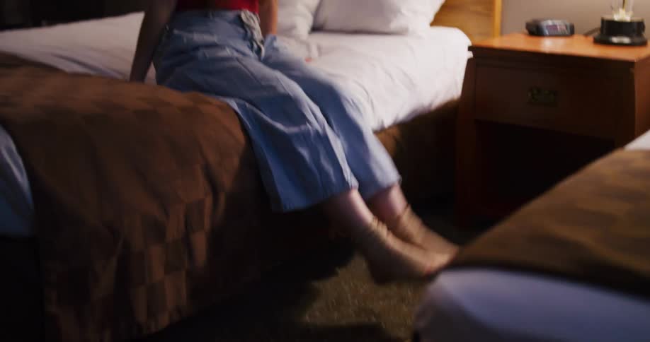 A happy woman in a sun hat playfully settles into her hotel room bed in slow motion, excited for her trip