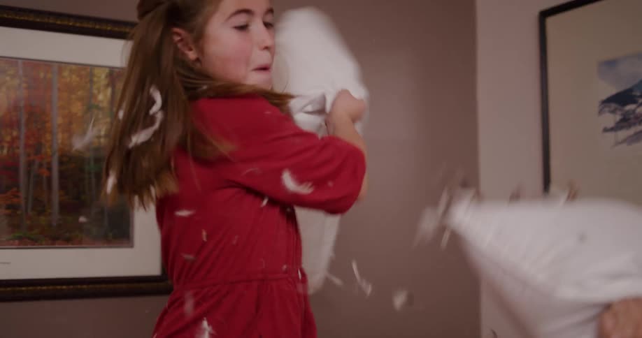 A young girl joyfully engages in a slow-motion pillow fight, sending feathers flying through the air
