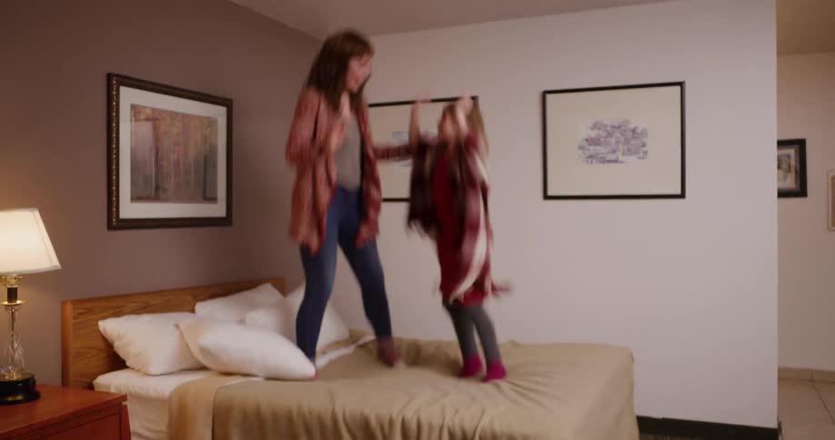 A carefree mother and daughter laugh and jump on a hotel bed in super slow motion