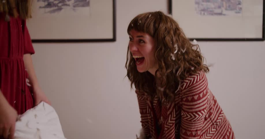 Two laughing young women have an epic pillow fight in slow motion as feathers explode and float through the air