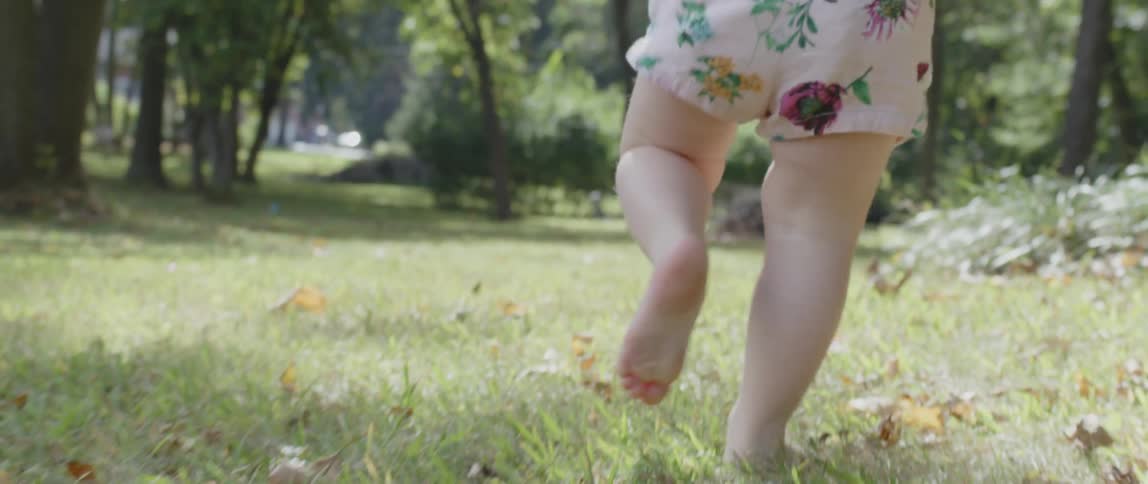 Toddler girl is running outside in grass and leaves on sunny day
