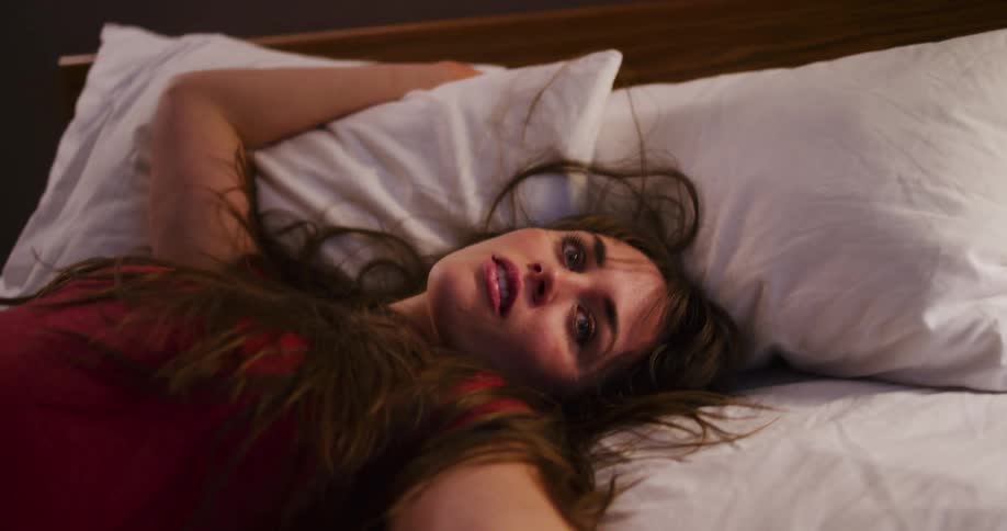 Exhausted and overwhelmed young woman lies on her bed in a dimly lit room in slow motion