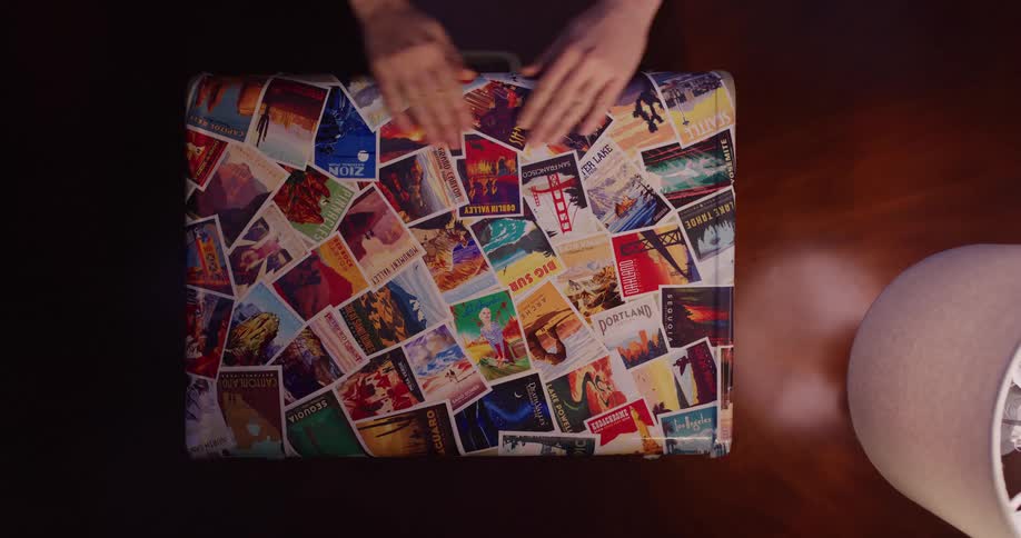 Top-down shot of hands reminiscing over a well-traveled suitcase covered in vintage postcards