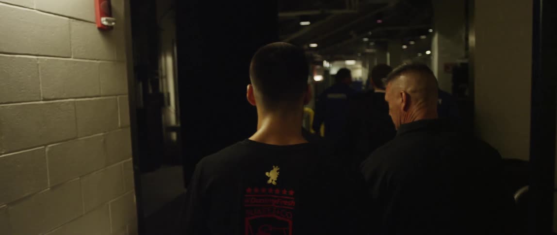 Group of men walking along a bricked hallway and into a parking garage