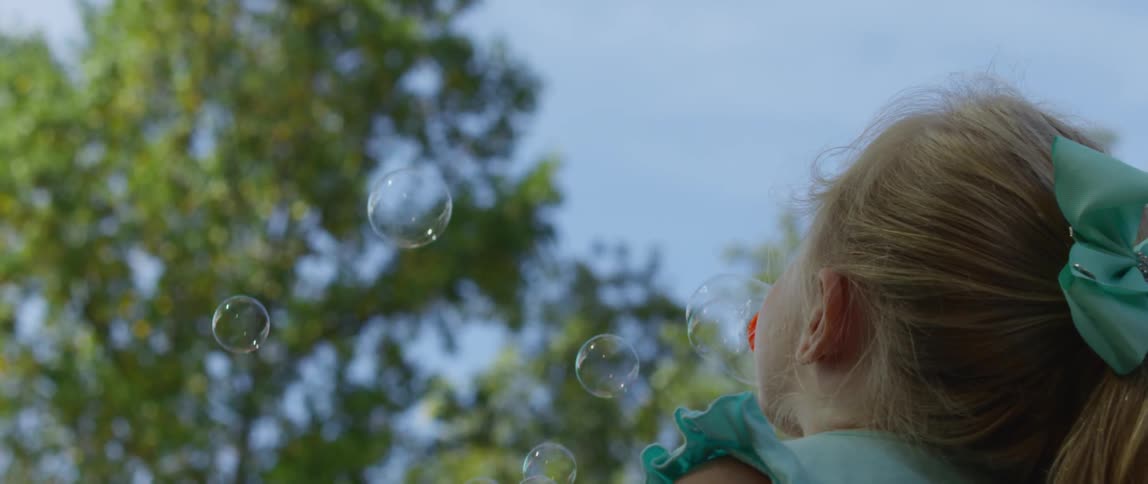 A little girl is blowing bubbles outside during the day