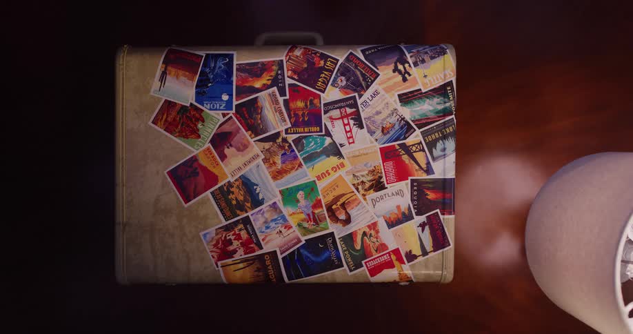 A looping animation of a vintage suitcase covered in colorful travel stickers resting on a wooden floor