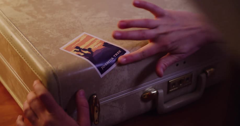 A traveler's hands smooth a Joshua Tree National Park sticker onto a vintage-style suitcase