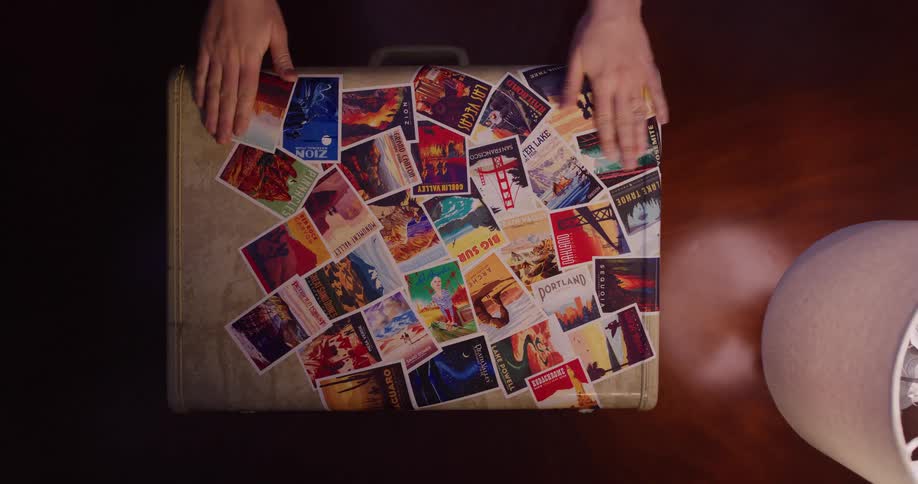 Overhead shot of hands securing a collage of colorful travel stickers onto a vintage suitcase, evoking a sense of wanderlust and cherished memories