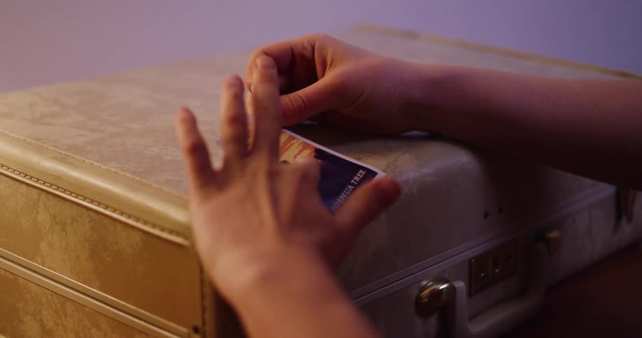 A person carefully places a Joshua Tree travel sticker onto their vintage suitcase in warm light