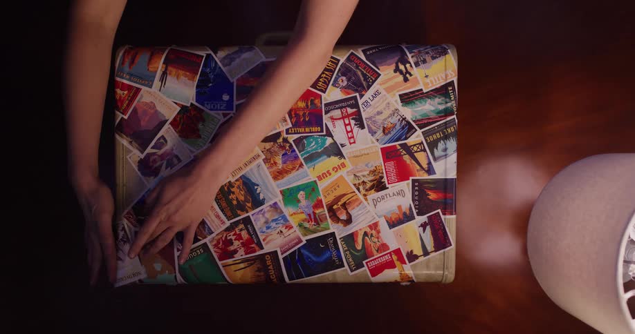 Overhead shot of a person's hands carefully applying colorful travel destination stickers to a suitcase, creating a collage of memories and adventures