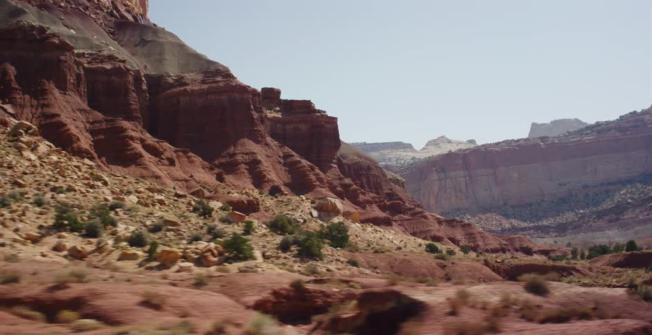 A slow tracking shot passes by towering red rock formations in a rugged desert canyon