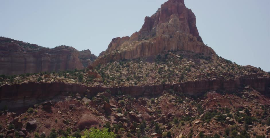 A slow pan reveals a majestic red rock mountain formation in a vast desert landscape on a sunny day