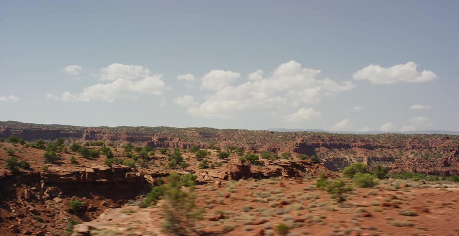 Driving through a stunning red rock desert canyon landscape on a sunny day with a few clouds in the sky