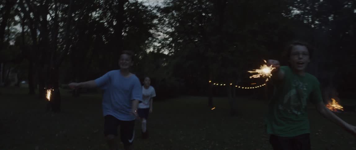 Children holding sparklers are running outside at dusk