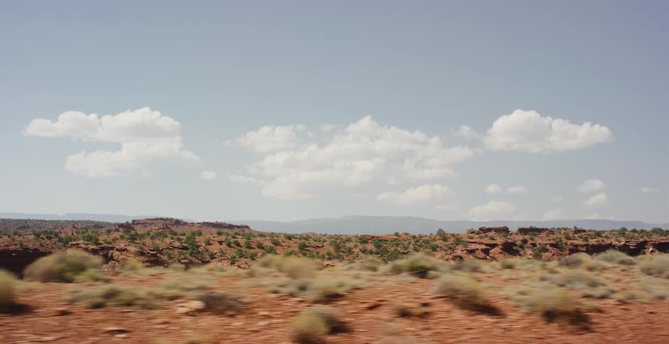 Driving through a vast desert landscape with red rock formations and sparse vegetation on a sunny day