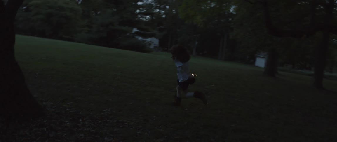 A young girl carrying a sparkler is running around a yard