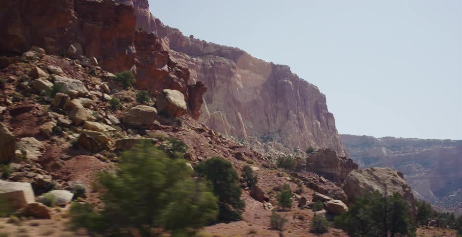 A slow-motion drive alongside the towering, sun-drenched red rock cliffs of a vast desert canyon