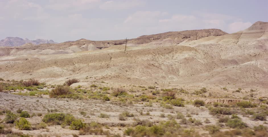 A slow dolly shot across a vast, arid desert landscape with rolling hills and sparse scrub brush on a hazy day