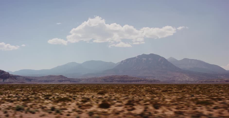 A fast-moving view of a vast desert landscape with distant mountains under a partly cloudy sky