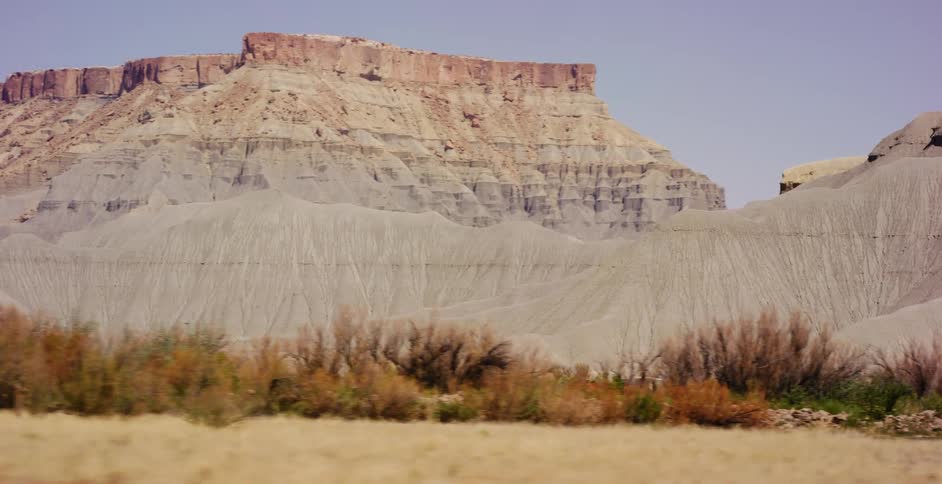 A tracking shot reveals the vast, arid landscape of a desert with majestic layered mesas under a hazy sky