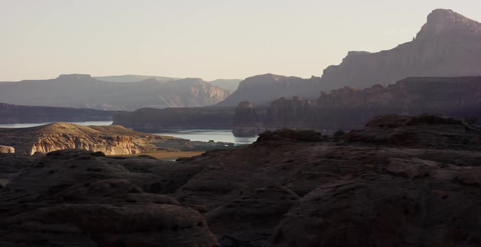 A slow dolly shot reveals the vast, rocky landscape and serene lake within a canyon at sunrise