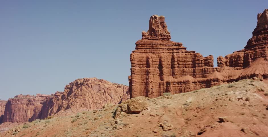 An aerial view slowly advances on a majestic red rock butte formation in the vast, arid desert landscape of southern Utah