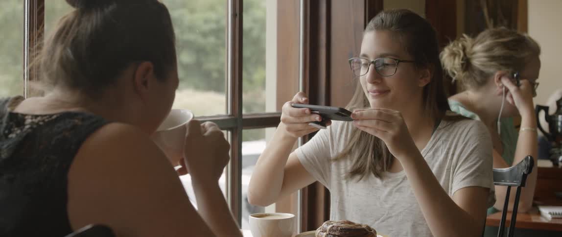 Two young women sitting at a table drinking coffee in taking pictures