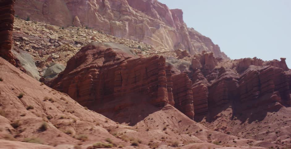 A smooth tracking shot reveals the vast, layered red rock formations of a sun-drenched desert canyon