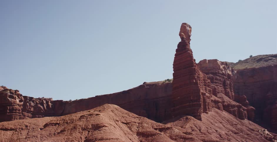 Driving shot past a stunning red rock spire and layered sandstone formations in the Utah desert