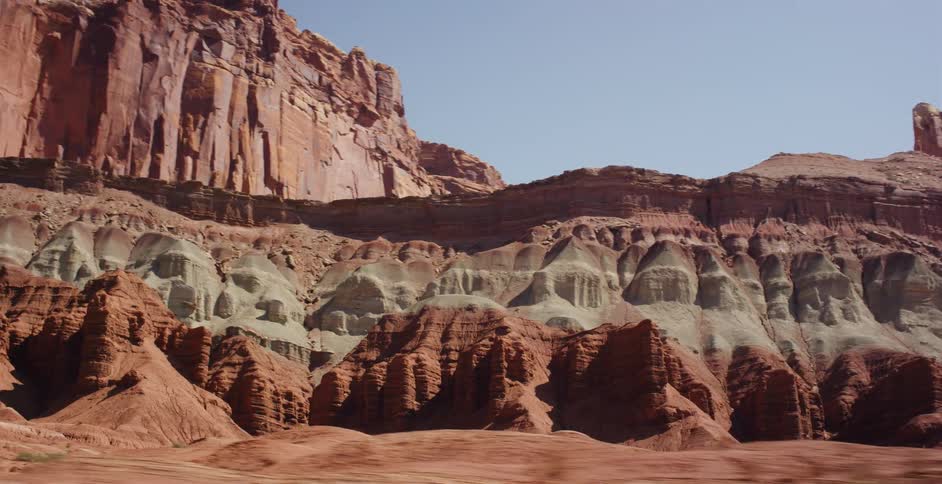 A scenic drive pans across the vibrant, multicolored rock formations and buttes of a vast desert landscape on a sunny day