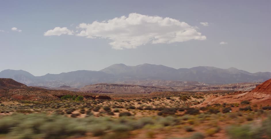 A fast-moving shot reveals a vast desert landscape with red earth, distant mountains, and a single cloud in the sky