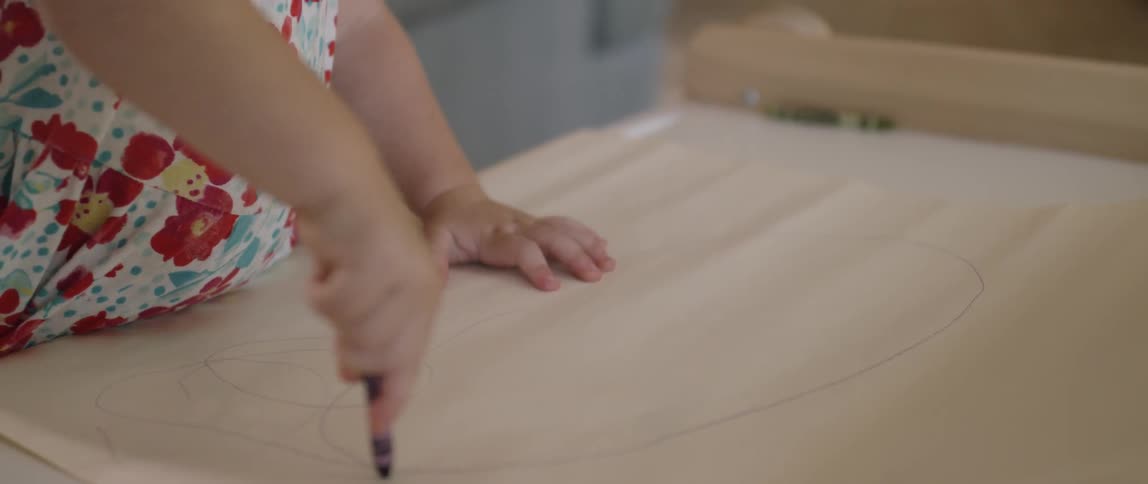 A young girl scribbles on a piece of paper with a crayon