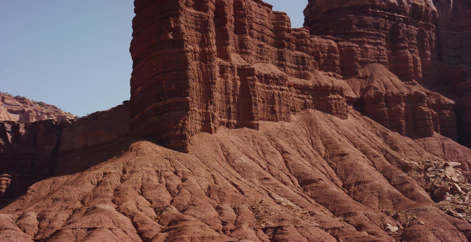 A cinematic aerial shot pulls back to reveal the impressive scale of the Chimney Rock formation in a vast, red desert canyon