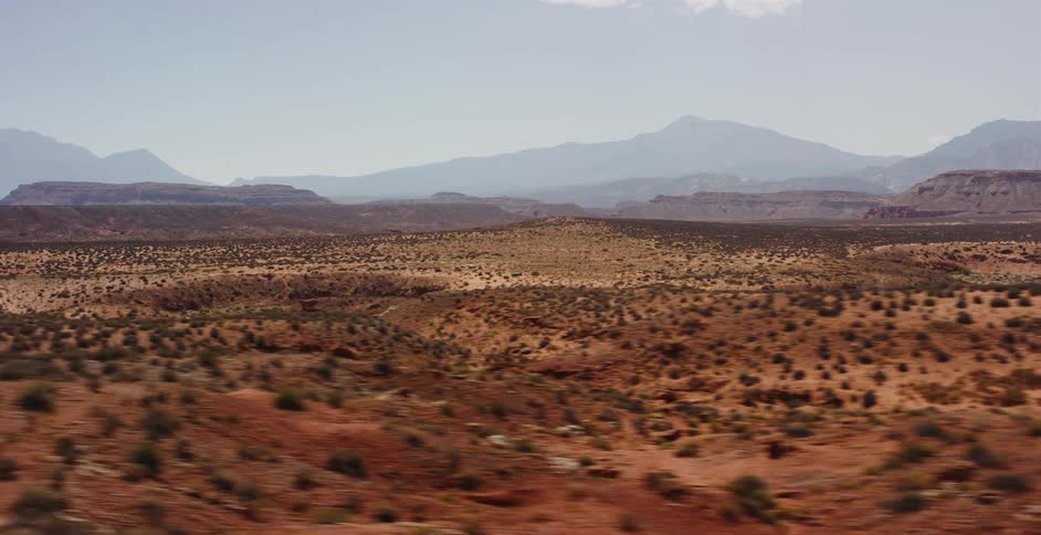 A sweeping aerial view pulls back over a vast, arid desert landscape with distant mountains on the horizon